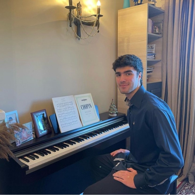 Adam Hartley sitting beside a piano